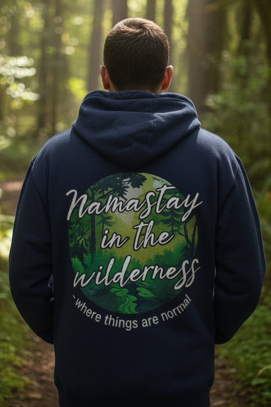 A navy blue pullover hoodie with a circular forest graphic on the chest. The graphic features the text 'Namastay in the wilderness' in white script over a green and yellow forest scene, with the phrase 'where things are normal' curved below it.