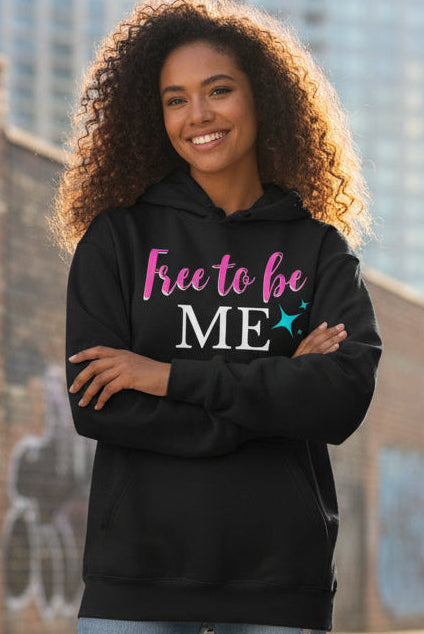 A black pullover hoodie with a front graphic that reads 'Free to be ME' in pink, white, and teal lettering, shown on a plain white background.