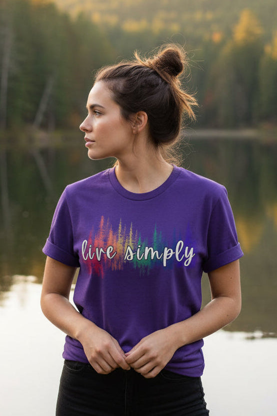 A purple short-sleeve crewneck t-shirt featuring a colorful graphic on the chest. The graphic displays a white script text reading 'live simply' overlaid on a vertical rainbow-colored soundwave design.
