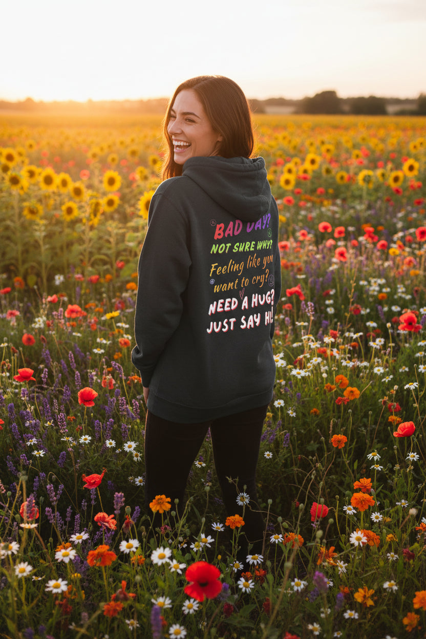 A dark charcoal gray zip-up hoodie shown from the back, featuring a colorful graphic text print that reads 'BAD DAY? NOT SURE WHY? Feeling like you want to cry? NEED A HUG? JUST SAY HI!' in pink, yellow, orange, and white lettering.