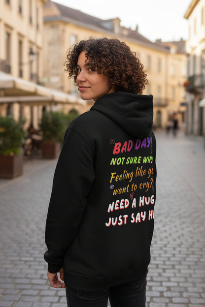 A black pullover hoodie shown from the back, featuring a colorful, playful text graphic that reads 'BAD DAY? NOT SURE WHY? Feeling like you want to cry? NEED A HUG? JUST SAY HI!' in various pastel and bright colors.
