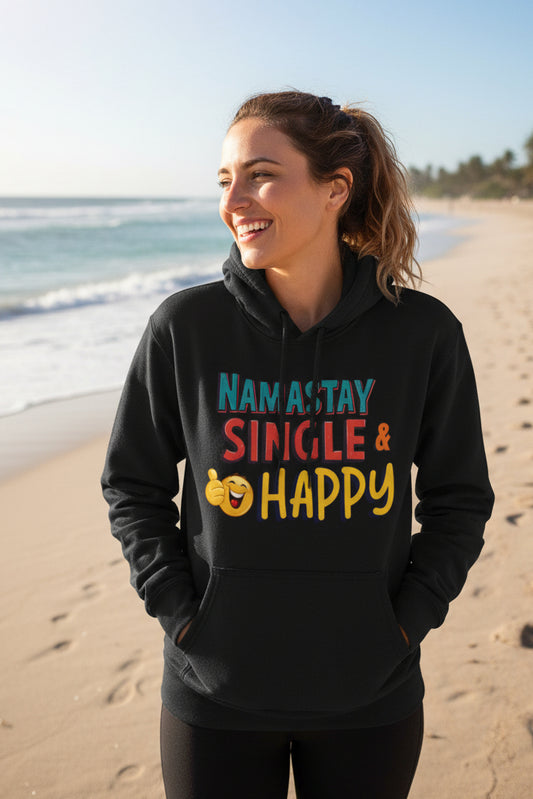 A black pullover hoodie with a colorful graphic on the chest that reads 'NAMASTAY SINGLE & HAPPY' in blue, red, and yellow lettering, accompanied by a yellow smiling emoji. The hoodie is shown against a plain white background.